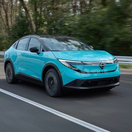 2025 Nissan Leaf electric vehicle driving on a two-lane road with trees in the background