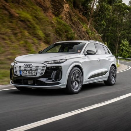 White Audi Q6 electric SUV cornering on a forest road with dynamic motion and sleek design