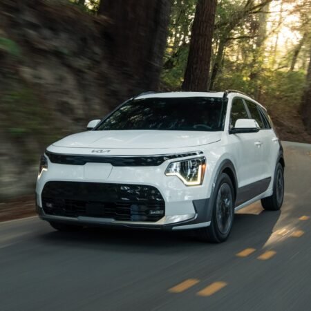 Front view of a white Kia Niro EV electric vehicle driving on a winding forest road with motion blur