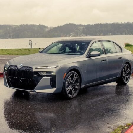 BMW 750e xDrive Plug-in Hybrid parked near a lake on a rainy day with wet pavement and cloudy sky